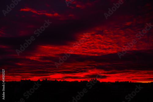 Colorful red sunrise over silhouette of city and dramatic sky with clouds - warm illumination, sun goes up. Nature, urban, morning, peaceful, atmospheric view concept © zyabich