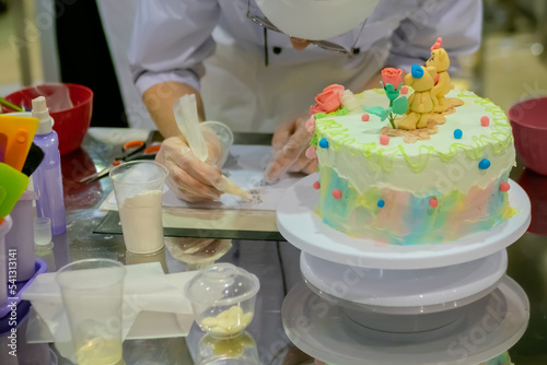 Chef, confectioner hands decorating child birthday dessert cake - close up. Professional cooking, bakery, cookery, gastronomy, pastry and food concept