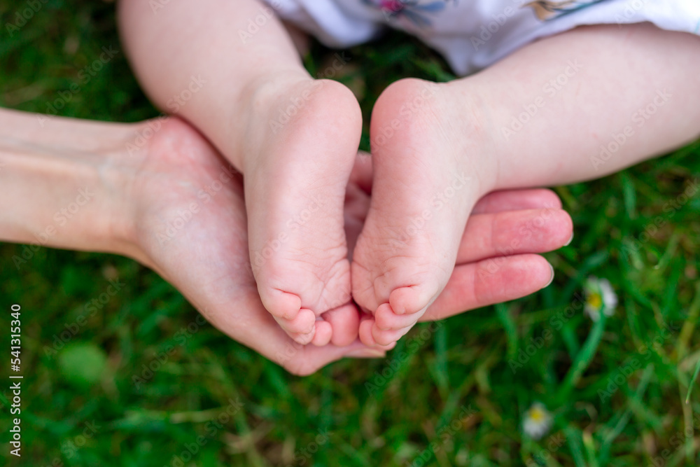 Children's feet on mother's palmon the background of grass