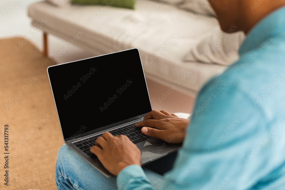 Fototapeta premium Young black guy in jeans typing on laptop with blank screen, chatting remotely in social networks