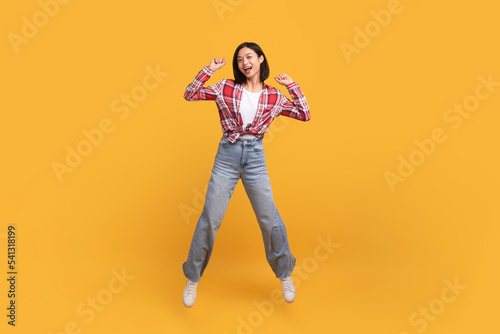 Euphoria concept. Full length shot of asian lady jumping and clenching fists isolated on yellow studio background