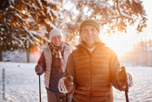 Waist up portrait of smiling mature couple enjoying Nordic walk in winter forest at sunset