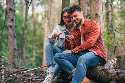 A couple is watching something funny on their smart phone during their rest after nature exploration and hiking, they look content and happy. © DusanJelicic
