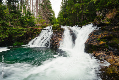 Strong stream of mountain waterfall in green forest - wide angle shot. Beautiful and power waterfall with turquoise water - stones and rocks on foreground.