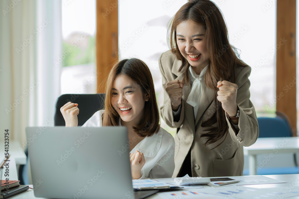 Two young Asian businesswomen look at their laptops and are overjoyed. successful new start project presentation of ideas and analyze financial planning and the investment market at the office. Two young Asian businesswomen look at their laptops and are overjoyed. successful new start project presentation of ideas and analyze financial planning and the investment market at the office.
