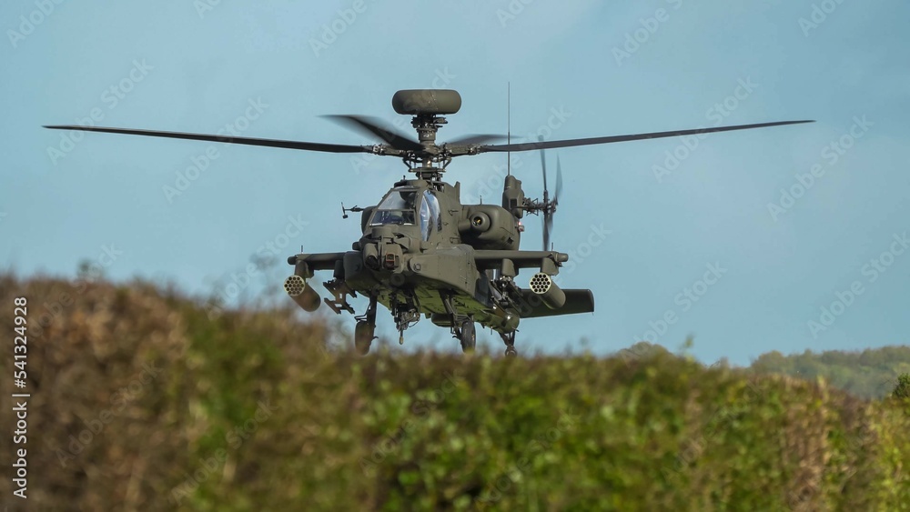 close-up head-on view of ZM707 British army Boeing Apache Attack helicopter (AH-64E ArmyAir606) sitting low behind hedgerow