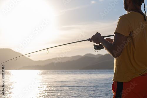 Young man fishing on a lake from the boat at sunset.reflection on water