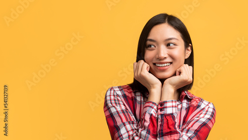 Great offer concept. Pretty asian lady touching her cheeks with hands and looking at copy space over yellow background