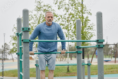 Front view portrait of determined mature man exercising on parallel bars outdoors, copy space