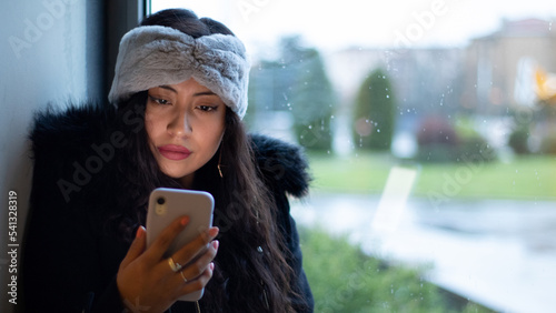 Pretty Latina girl shopping in a mall, reading her cell phone screen and wearing a hair band.