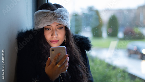 Pretty Latina girl shopping in a mall, reading her cell phone screen and wearing a hair band.
