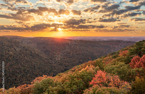 Sun setting behind clouds illuminating the fall colors of the trees in Coopers Rock State Forest