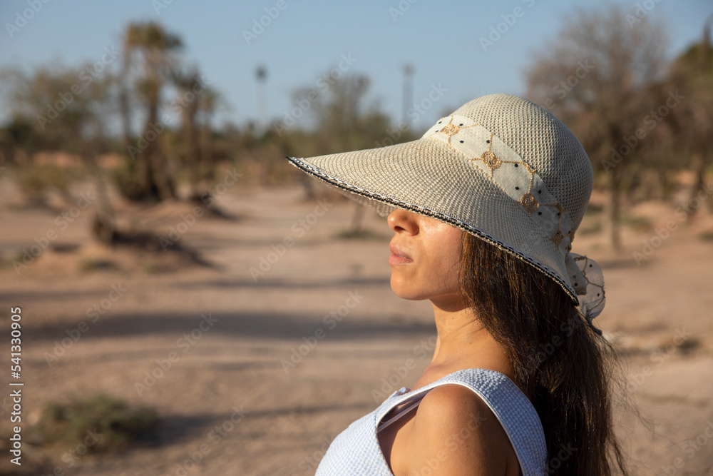 Sexy tourist with hat enjoying sitting in the desert landscape and palm trees that offers the city of Marrakech in its palm grove, this place is very visited in Morocco by tourists.