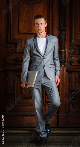 Obraz na płótnie Young Eastern European Businessman working in New York City, wearing gray fashionable suit, black leather shoes, carrying laptop computer, walking down stairs of office doorway. . w salonie