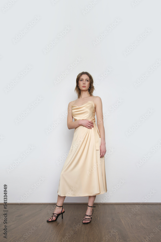 Female model wearing beige camisole silk top and wrapped midi skirt. Stylish and elegant monochrome summer outfit. Fashion Studio shot. Female model wearing beige camisole silk top and wrapped midi skirt. Stylish and elegant monochrome summer outfit. Fashion Studio shot.
