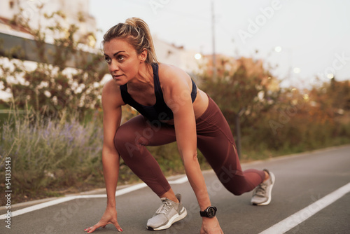 Mature woman in a starting position ready to start running fast, sprinter, exercising and working out