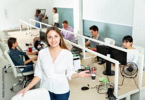 Smiling happy cheerful positive female manager standing in open space office during working process