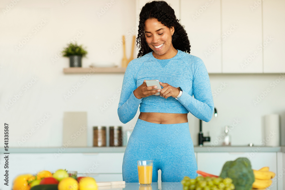 Fitness black blogger woman using smartphone for chatting and checking social media in the kitchen