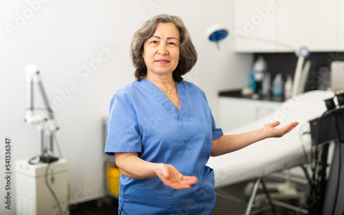 Portrait of an experienced female doctor standing in an workroom in a clinic in a good mood