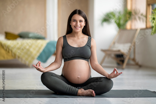 Smiling Young Pregnant Female Meditating On Fitness Mat At Home