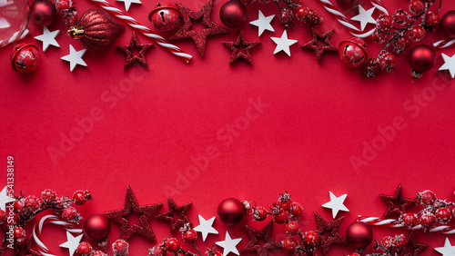 Merry Christmas and Happy New Year banner concept.Close-up red christmas balls,striped lollipops, stars,branches with berries on red background,flat lay,top view,space for text.Festive decor,postcard.