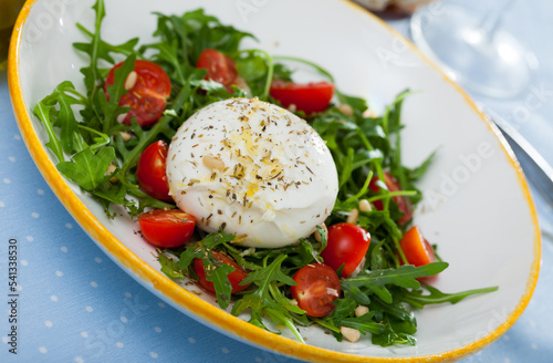Close up of salad with burrata italian cheese, cherry tomatoes and arugula green leaf at plate