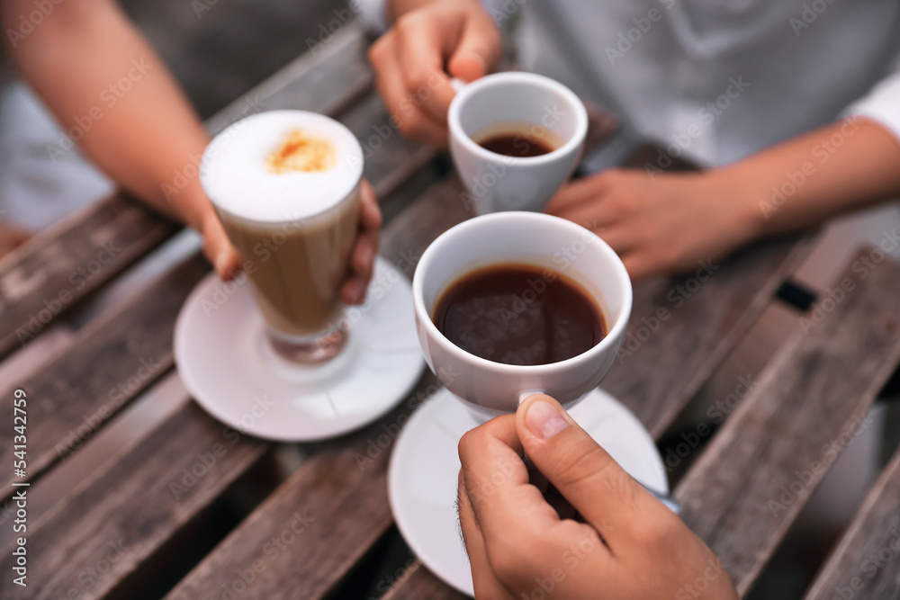 Friends drinking coffee at wooden table in outdoor cafe, closeup Friends drinking coffee at wooden table in outdoor cafe, closeup