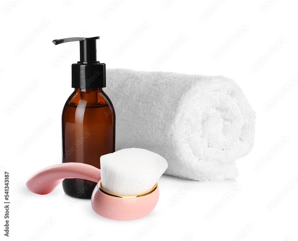 Rolled clean towel, bottle of hydrophilic oil and face cleansing brush on white background