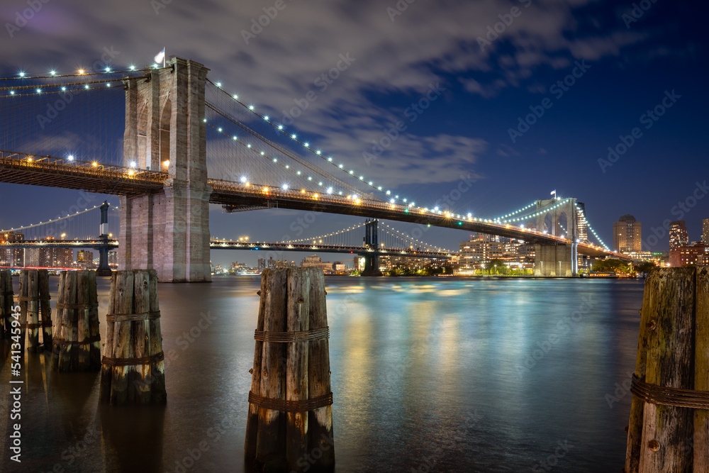 Evening view of the Brooklyn Bridge and Manhattan Bridge and wood pilings. View of East River and Dumbo in Brooklyn, New York City