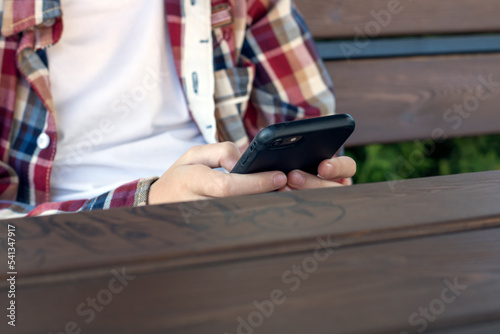 Phone in hand close-up, typing a message on social networks. A teenager sits with a phone in his hand © Marina