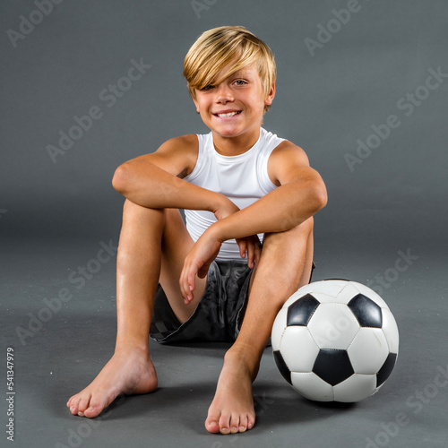 фотографія Happy young soccer player sitting barefoot on the ground with his soccer ball