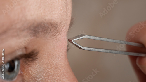 woman plucking eyebrows with tweezers closeup