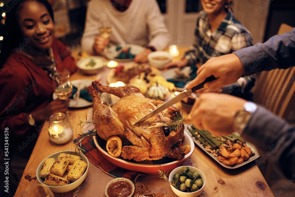 Close up of man carving turkey meat while having dinner with friends on Thanksgiving. - obrazy, fototapety, plakaty 