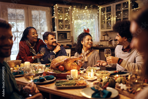 Multiracial group of friends have fun while talking during Thanksgiving dinner at dining table.