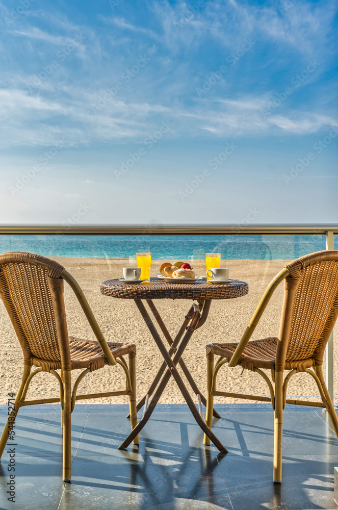 Table with breakfast and two chairs on a hotel balcony by the beach - Travel concept