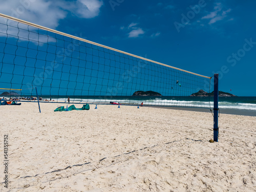 Volleyball net or futvolei on the sand of Barra da Tijuca beach, Rio de Janeiro, Brazil. Sunny day with blue sky and some clouds. Windsurfing at sea.
