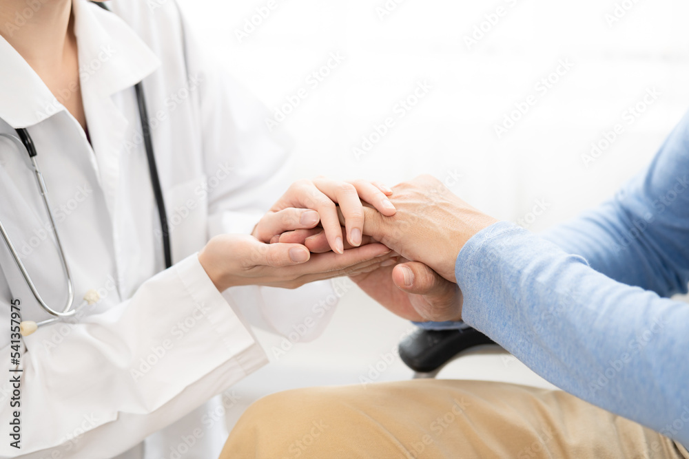 Female doctor hand taking care and talking senior male patient sitting on chair in hospital. Healthcare concept.