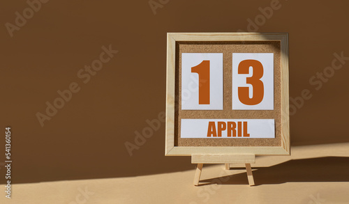 April 13th. Day 13 of month, Calendar date. Cork board, easel in sunlight on desktop. Close-up, brown background. Spring month, day of year concept