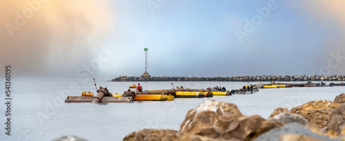 Ocean dredger pipes in the ocean near the harbor entrance with sea lions sitting on top and birds on harbor wall Oxnard California
