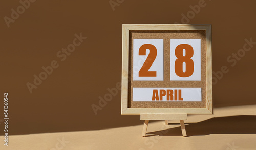 April 28th. Day 28 of month, Calendar date. Cork board, easel in sunlight on desktop. Close-up, brown background. Spring month, day of year concept photo