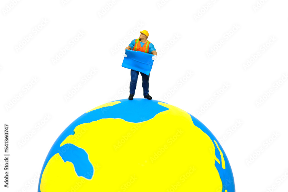 Miniature people toy figure photography. Project location concept. A construction worker holding blueprint standing above earth globe. Isolated on white background Miniature people toy figure photography. Project location concept. A construction worker holding blueprint standing above earth globe. Isolated on white background