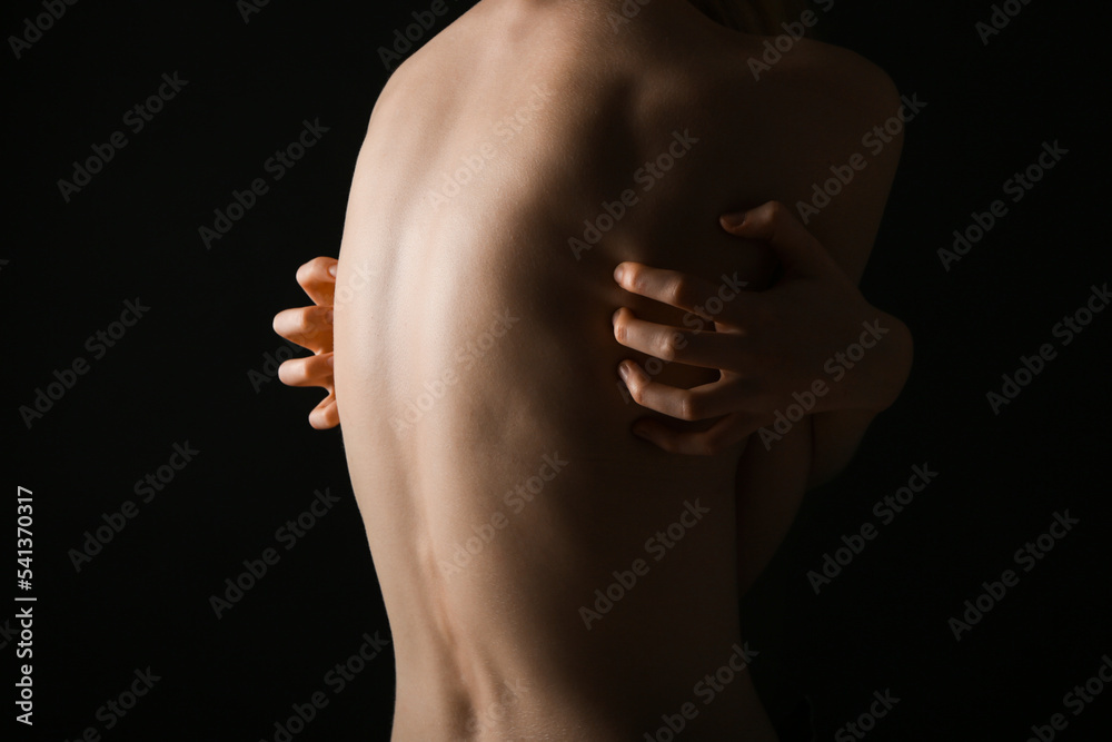 Back of young woman on dark background. Anorexia concept