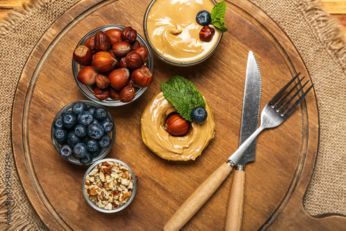 Wooden board with tasty apple round, nut butter, blueberry and hazelnuts on table, closeup