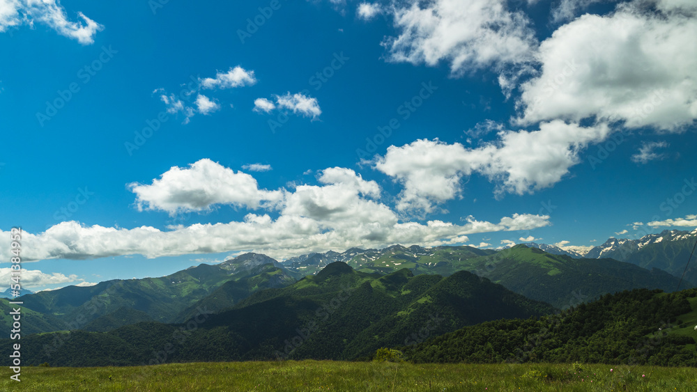 Mountain peaks hills and mountain passes. Blue sky with clouds. Part of the mountains are covered with remnants of snow. Mountain summer landscape.