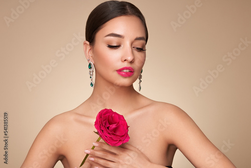 A beautiful young woman with shiny brunette hair. Girl with a rose flower. Model with healthy skin. Cosmetology  beauty and spa