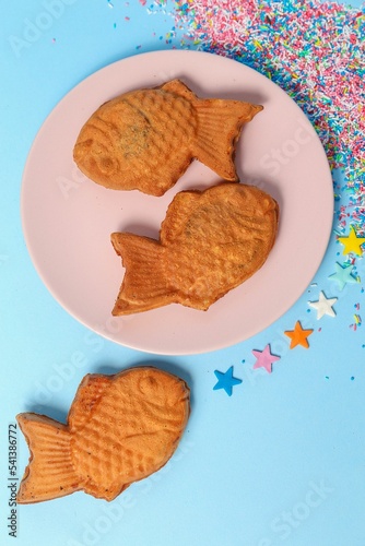 Vertical top view of fish-shaped Taiyaki ice cream cones in a pink plate over the blue surface