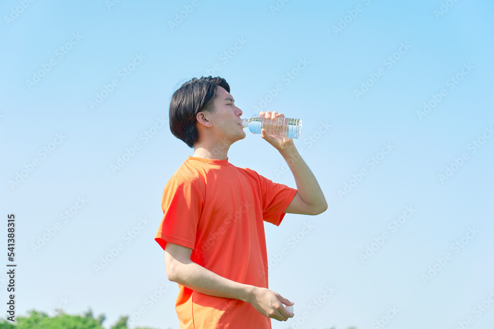 外で運動中に水分補給する男性 外で運動中に水分補給する男性