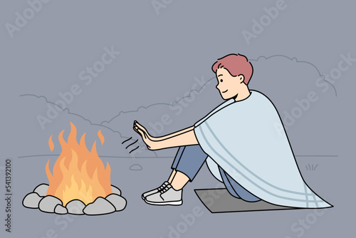 Young man sit on ground in nature warm hands at campfire at night. Smiling male relax on hiking trip in forest near fire. Vector illustration. 
