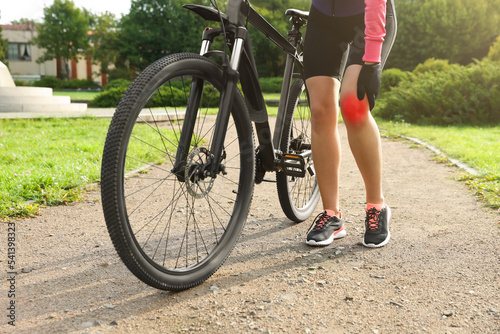 Woman with injured knee and bicycle outdoors, closeup