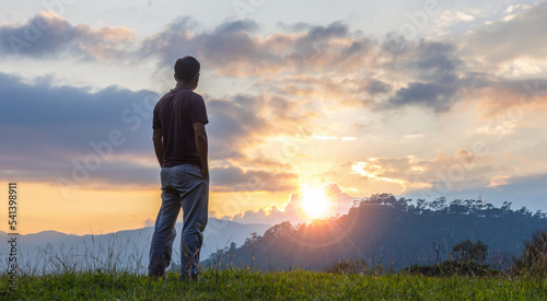 Man standing on a mountain hill at sunset and enjoying view of nature